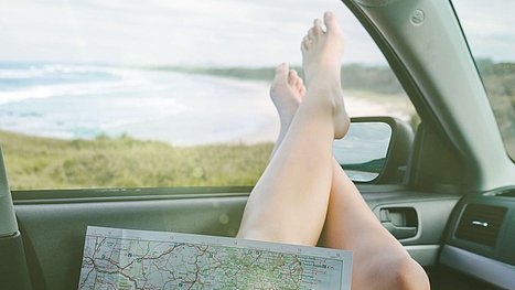 Frau streckt Beine aus offenem Autofenster mit Landkarte auf dem Schoss.