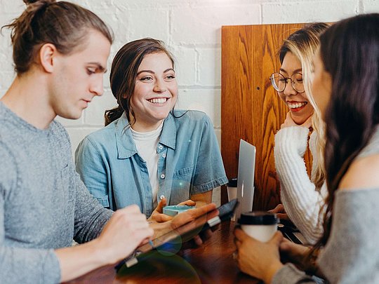Drei Frauen und ein Mann unterhalten sich und lächeln