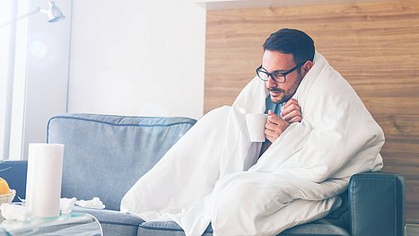 Mann sitzt mit einer Decke über den Schultern auf der Couch