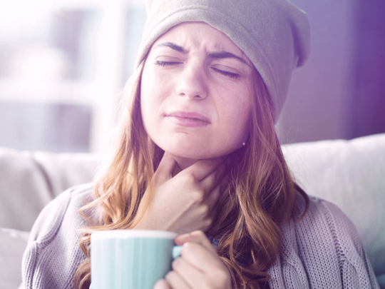Frau greift sich mit der Hand an den Hals und hält eine Tasse in der Hand