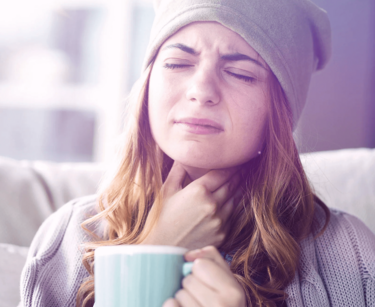 Frau greift sich mit der Hand an den Hals und hält eine Tasse in der Hand