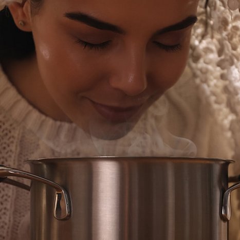 Inhalieren kann eine gesunde Stimme unterstützen. Frau inhaliert Wasserdampf aus einem Topf.