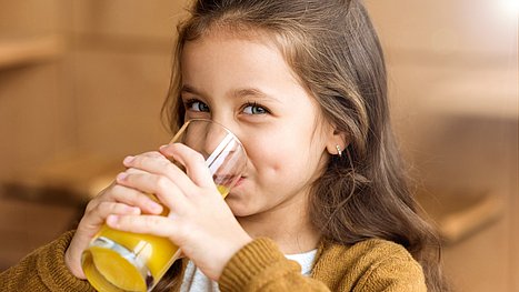 Wie lassen sich Husten, Halskratzen und Co. bei Kindern vorbeugen? Junges Mädchen trinkt Orangensaft.