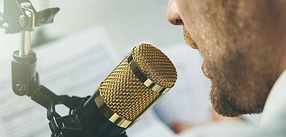 Ein vorübergehender Verlust der Stimme wird auch Aphonie genannt. Mann spricht in ein Mikrofon.