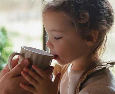Halsschmerzen bei kleinen Kindern kann durch Halsliquid gelindert werden. Vater gibt seinem Kind ein Getränk gegen Halsschmerzen bei Kindern.